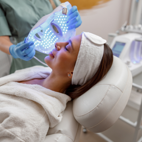 woman laying on a white chair as someone is about to put an LED light mask on her.