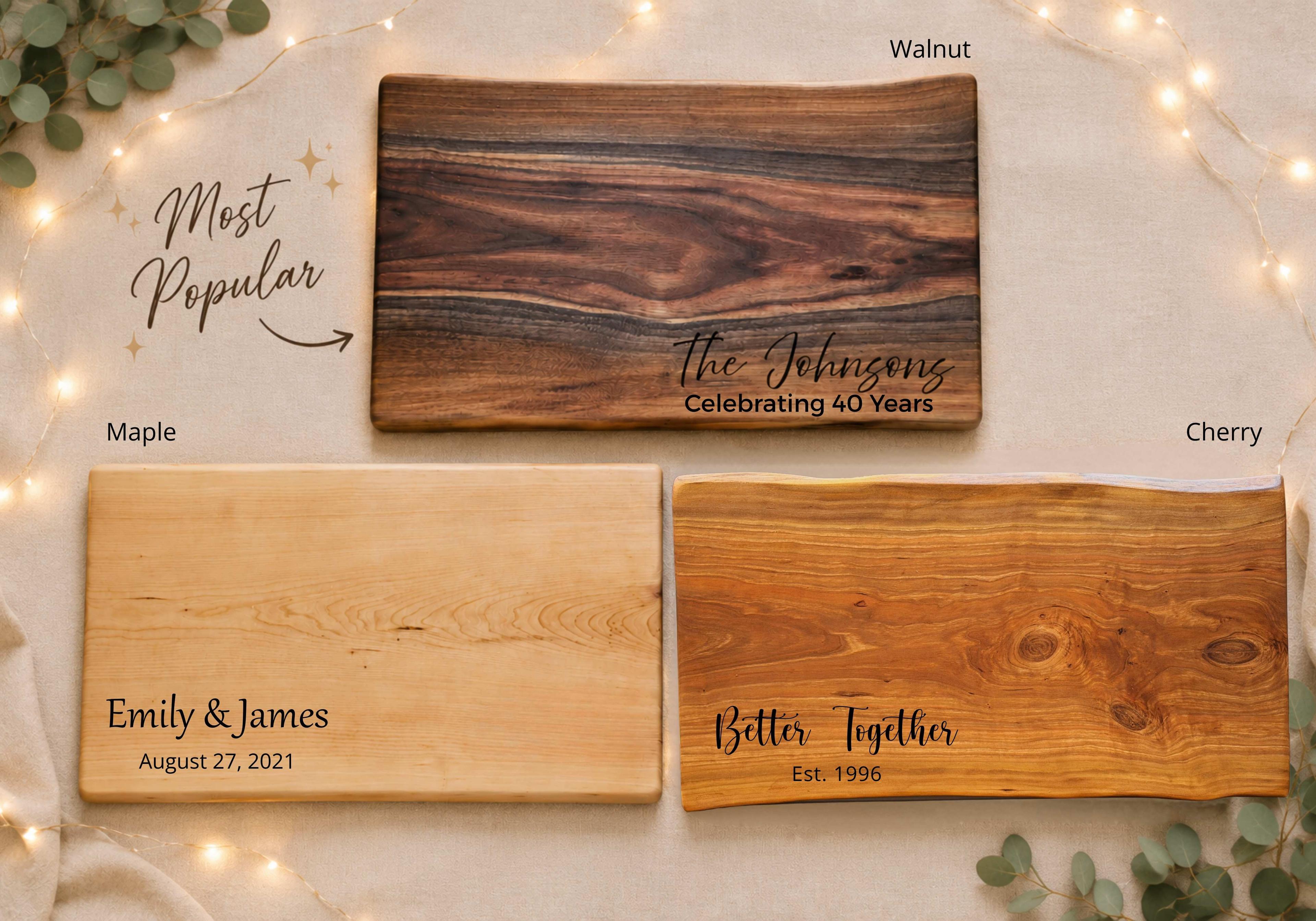Create a warm, premium anniversary engraving inspiration image featuring three personalized hardwood boards crafted from walnut, maple, and cherry. Example engraving 1: The Johnsons Example engraving 2: Emily & James August 27, 2021 Example engraving 3: Our Story Continues Celebrating 40 Years Example engraving 4: Forever & Always The image should feel elegant, gift-focused, and suitable for an anniversary gift guide. Use soft lighting, warm tones, and a premium handcrafted aesthetic. Make the engraving examples large enough to read clearly while showcasing the natural beauty of the wood grain. The overall purpose is to help customers visualize popular anniversary engraving styles including family names, names and dates, milestone anniversaries, and meaningful romantic phrases.