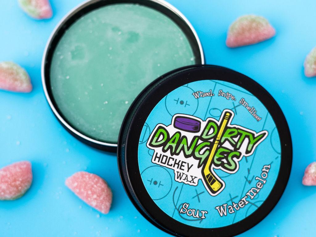 An open tin of dirty dangles sour watermelon hockey stick wax on a blue background with sour watermelon candies
