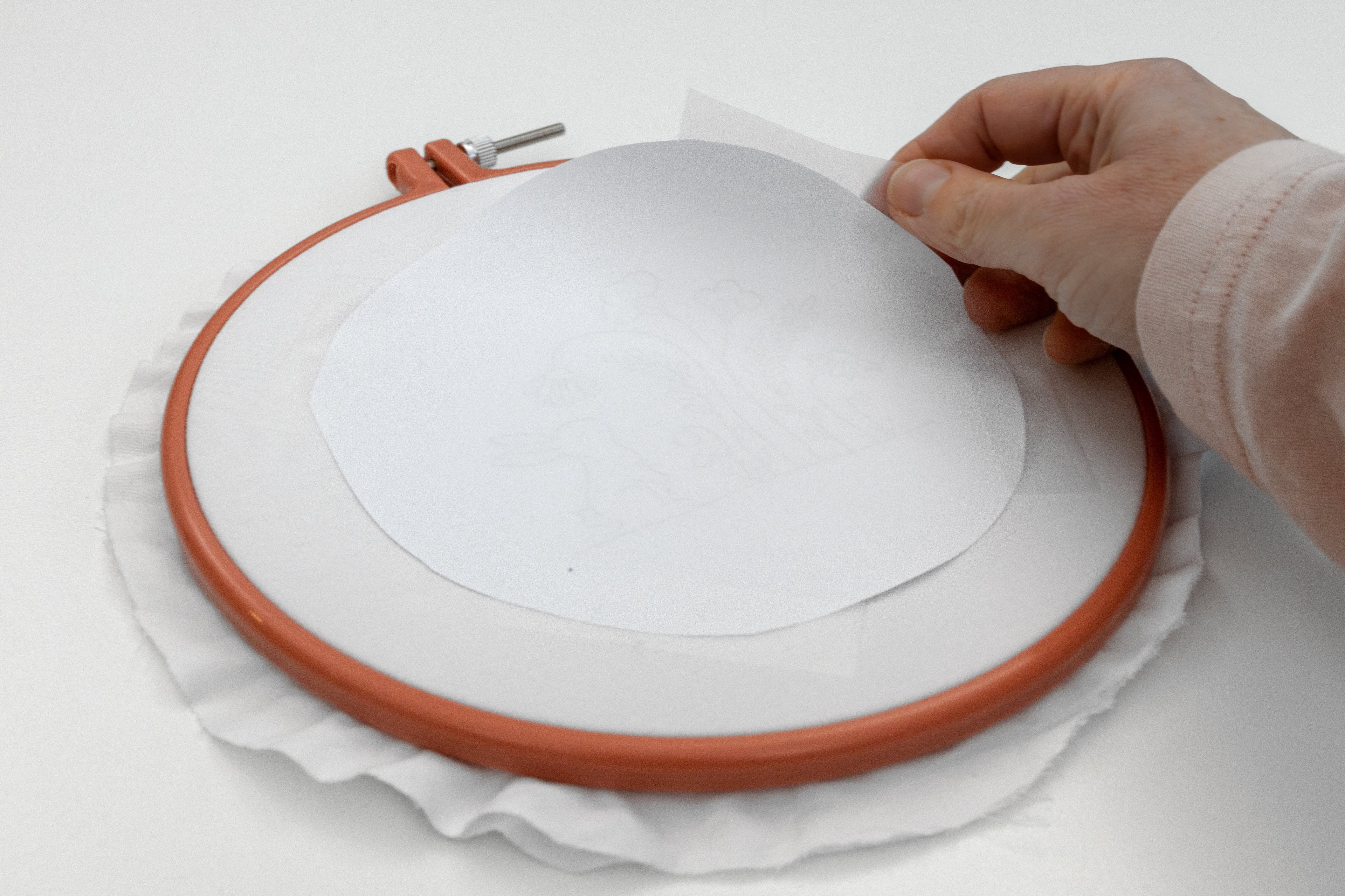 A hand cellotapes the pattern onto the blank hoop.