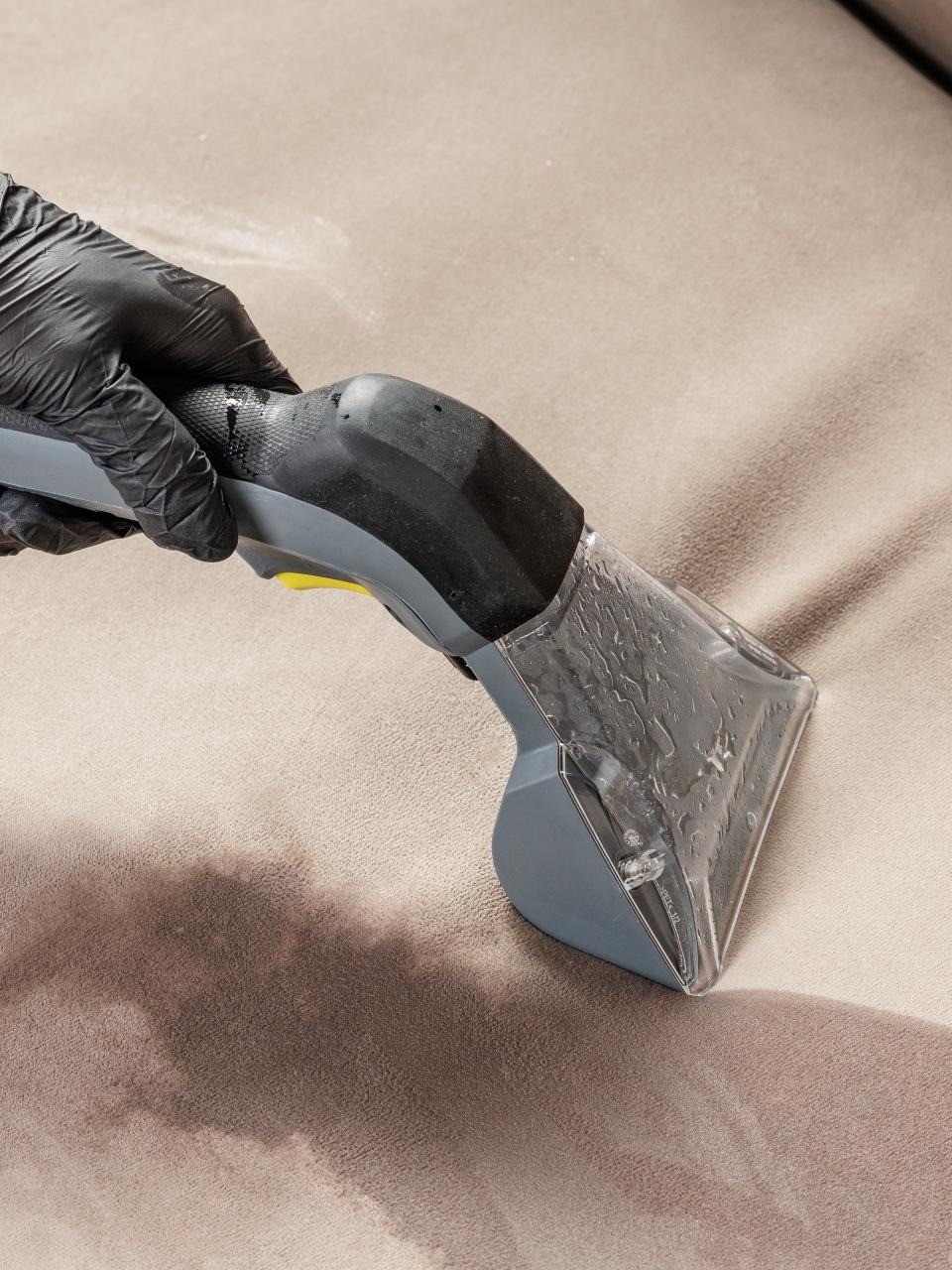 Gloved worker uses an upholstery extractor to remove a wet stain from a sofa seat