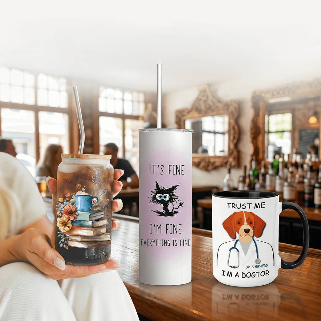 Dog-themed ceramic mug and ‘It’s Fine’ stainless steel tumbler displayed on a wooden desk in a cozy library setting.