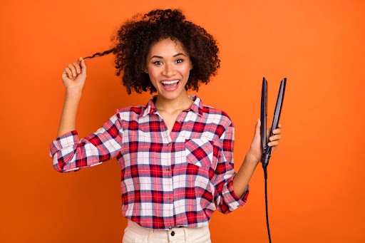 black woman with natural hair holding a flat iron for a silk press