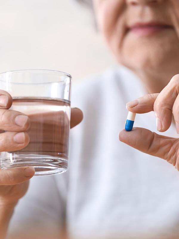 close-up of elderly woman holding a glass of water and a pill