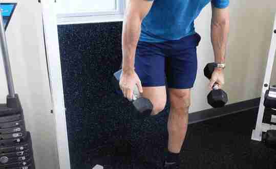 Man In Blue with Shorts Holding Dumbbells in Gym Outside View
