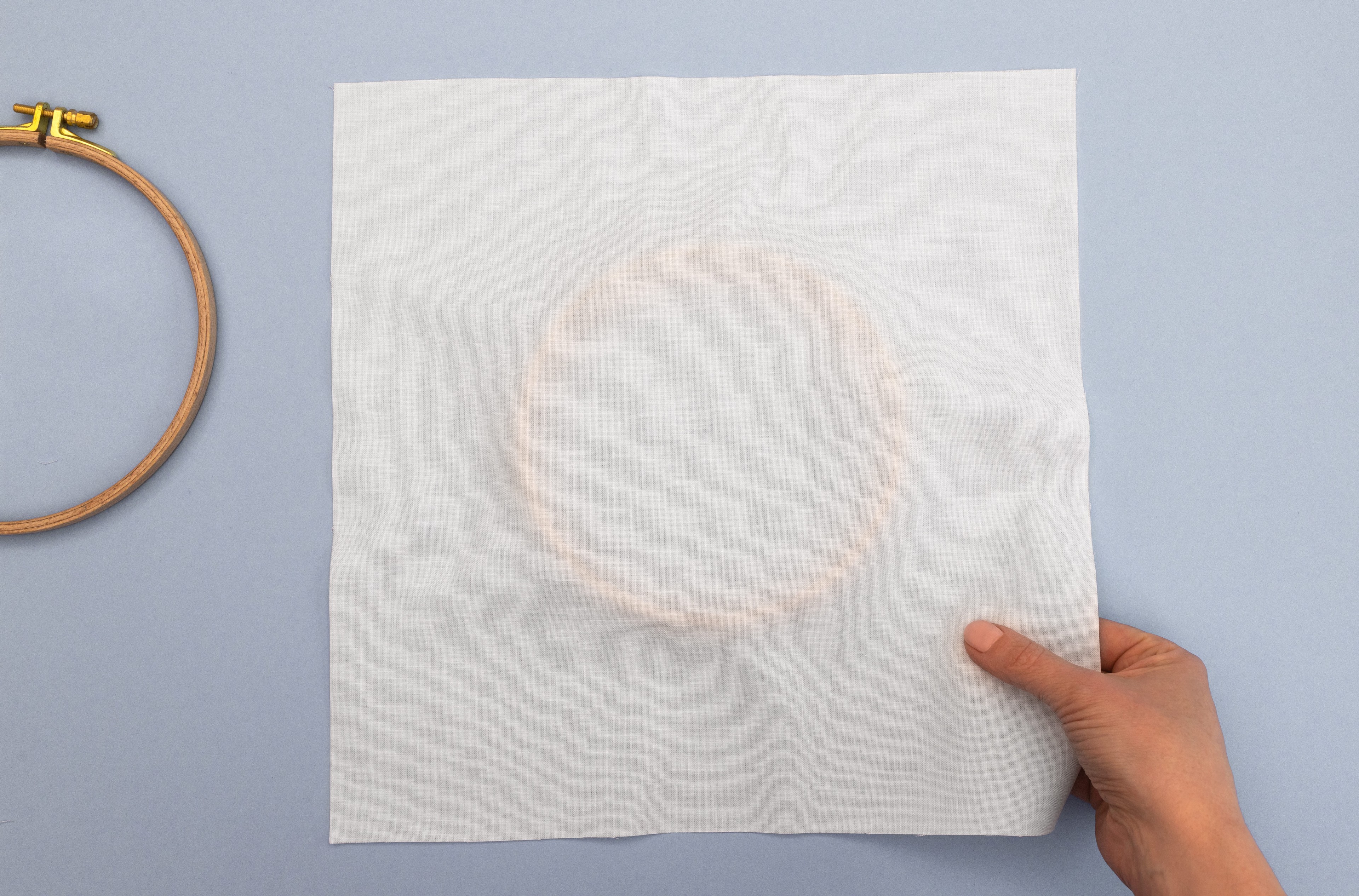 A hand holds fabric over a hoop.