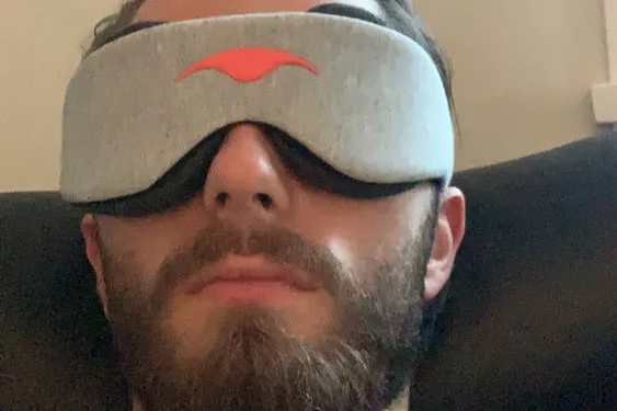 A man relaxing and wearing a gray eye mask with contoured eye cups.