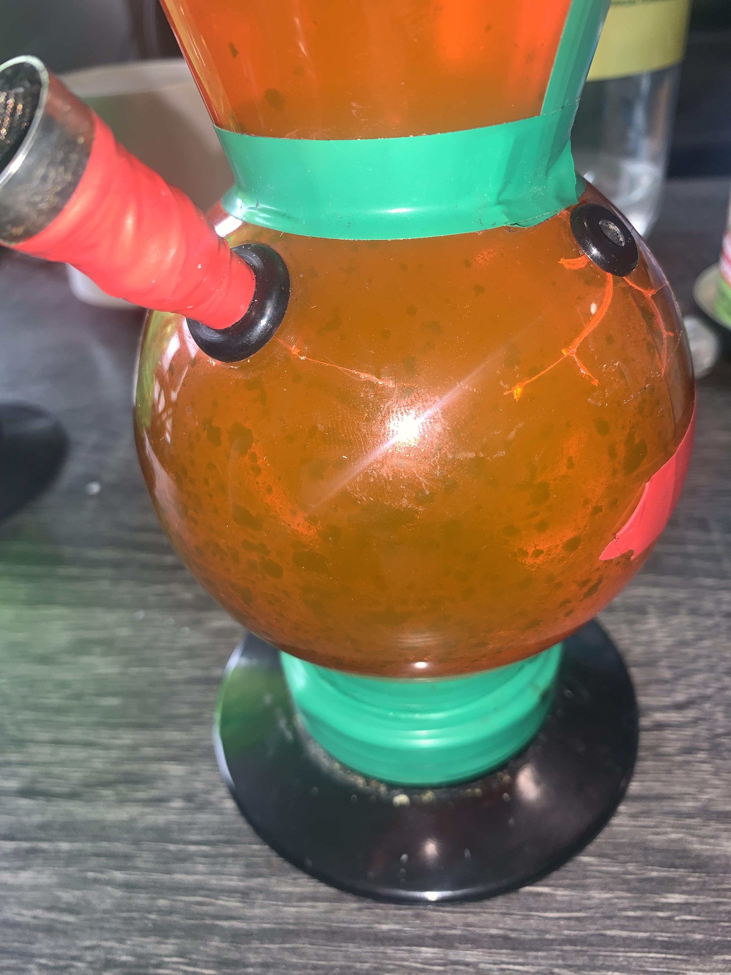 Close-up photo of a deeply worn, decaying orange acrylic bong held together with duct tape. This image clearly illustrates "acrylic decay," showing the material breakdown, discoloration, and structural failure that highlights the long-term safety risks and short lifespan of cheap plastic smoking pipes.