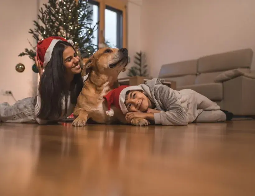 A woman and two children in pajamas relax on the floor with a dog, creating a cozy family scene.