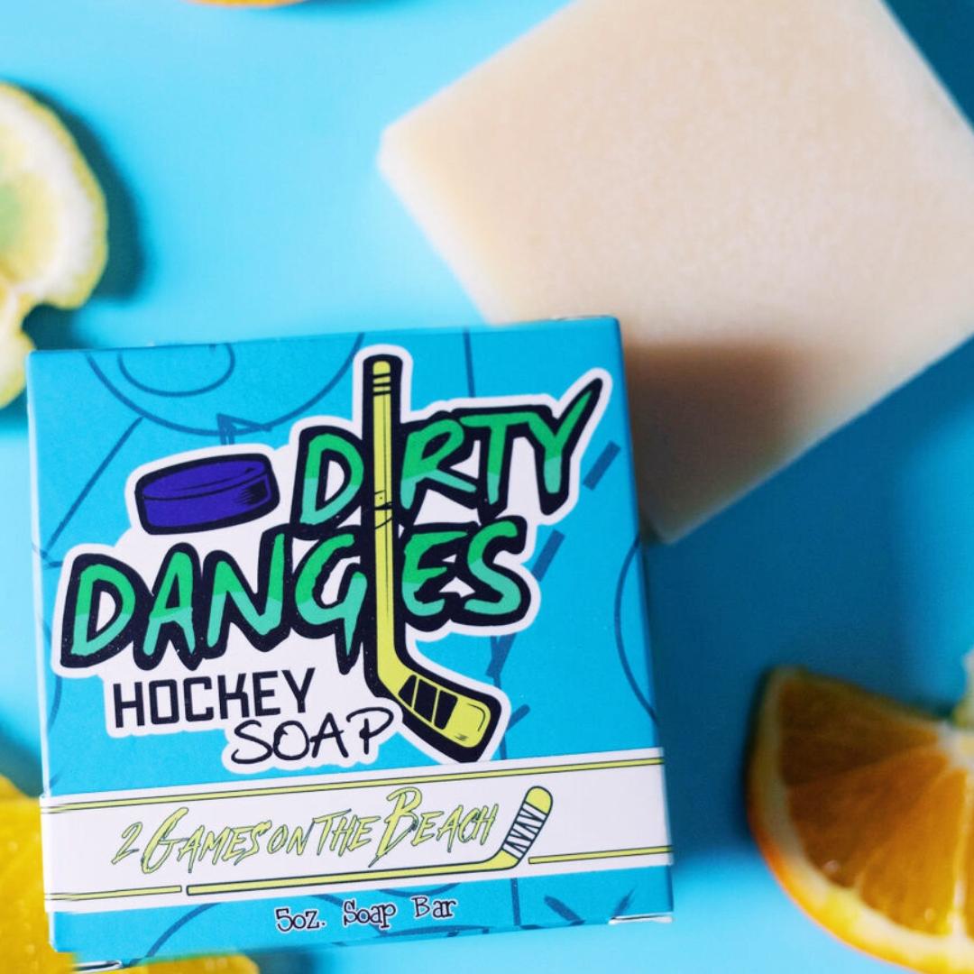 A yellow 2 games on the beach hockey soap bar on a blue background with a blue box, lemons and lavender