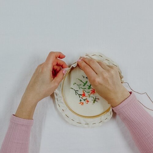 A hand sews around the outside of the fabric, preparing to frame an embroidery creation.