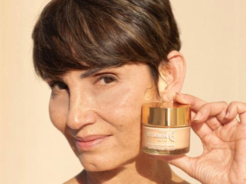 woman holding Noche's Vitamin C Face Cream up next to her cheek.