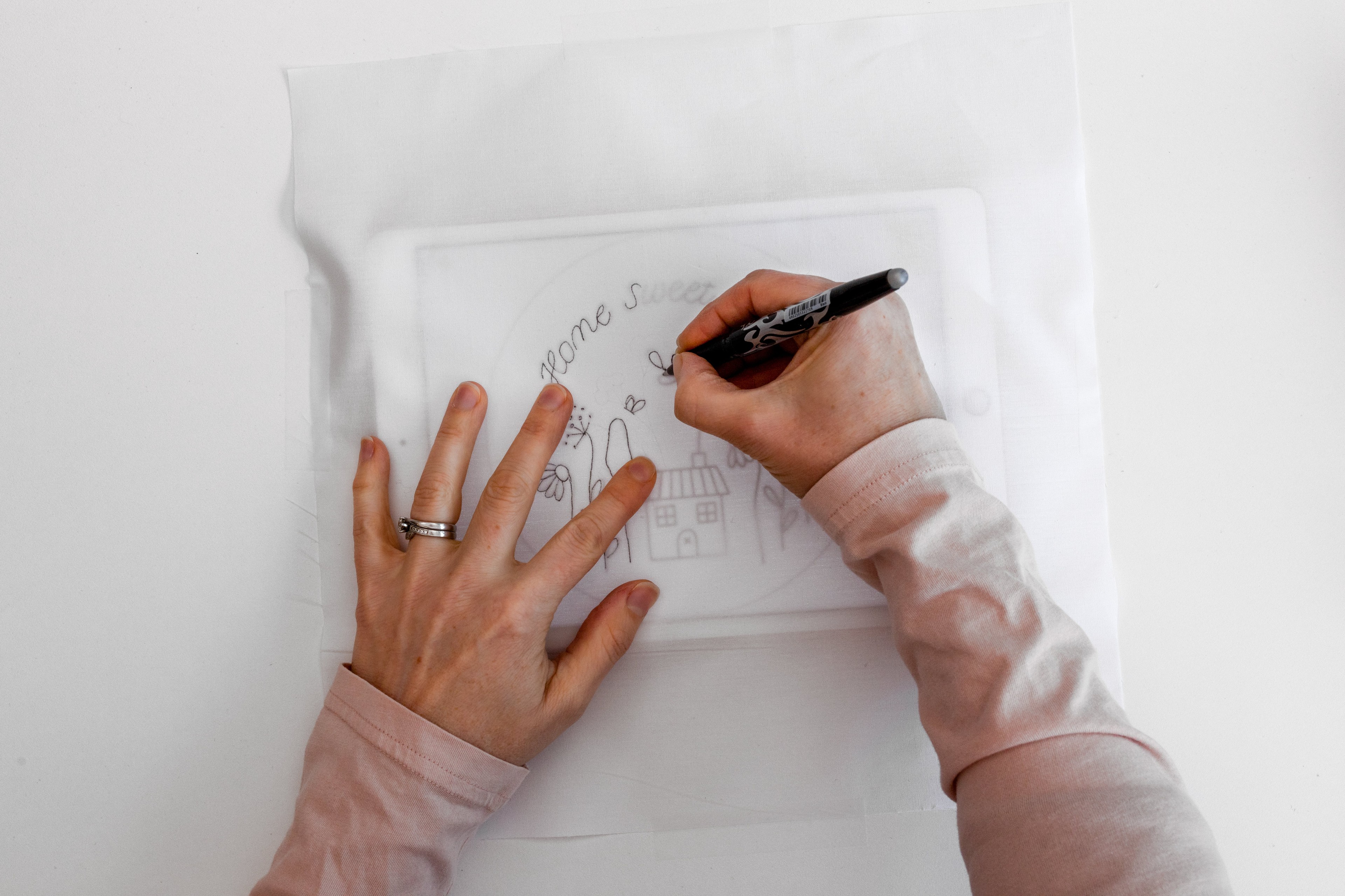 A hand draws a pattern on fabric using a tablet as a light source.