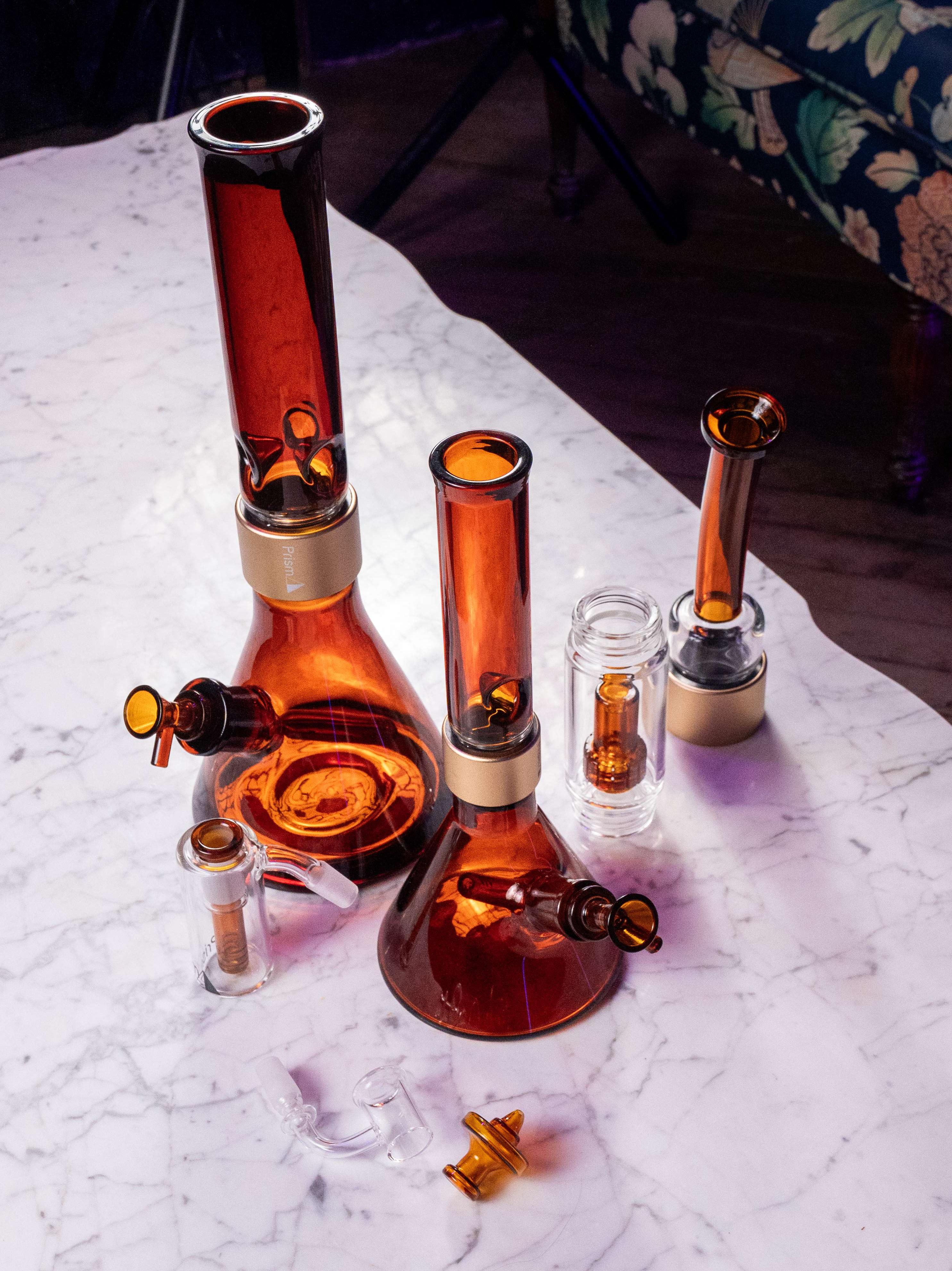 A collection of Prism Amber glass accessories and modular parts, featuring amber ash catchers, showerhead percolators, bent mouthpieces, 14mm bowls, and angular carb caps for the modular halo system.